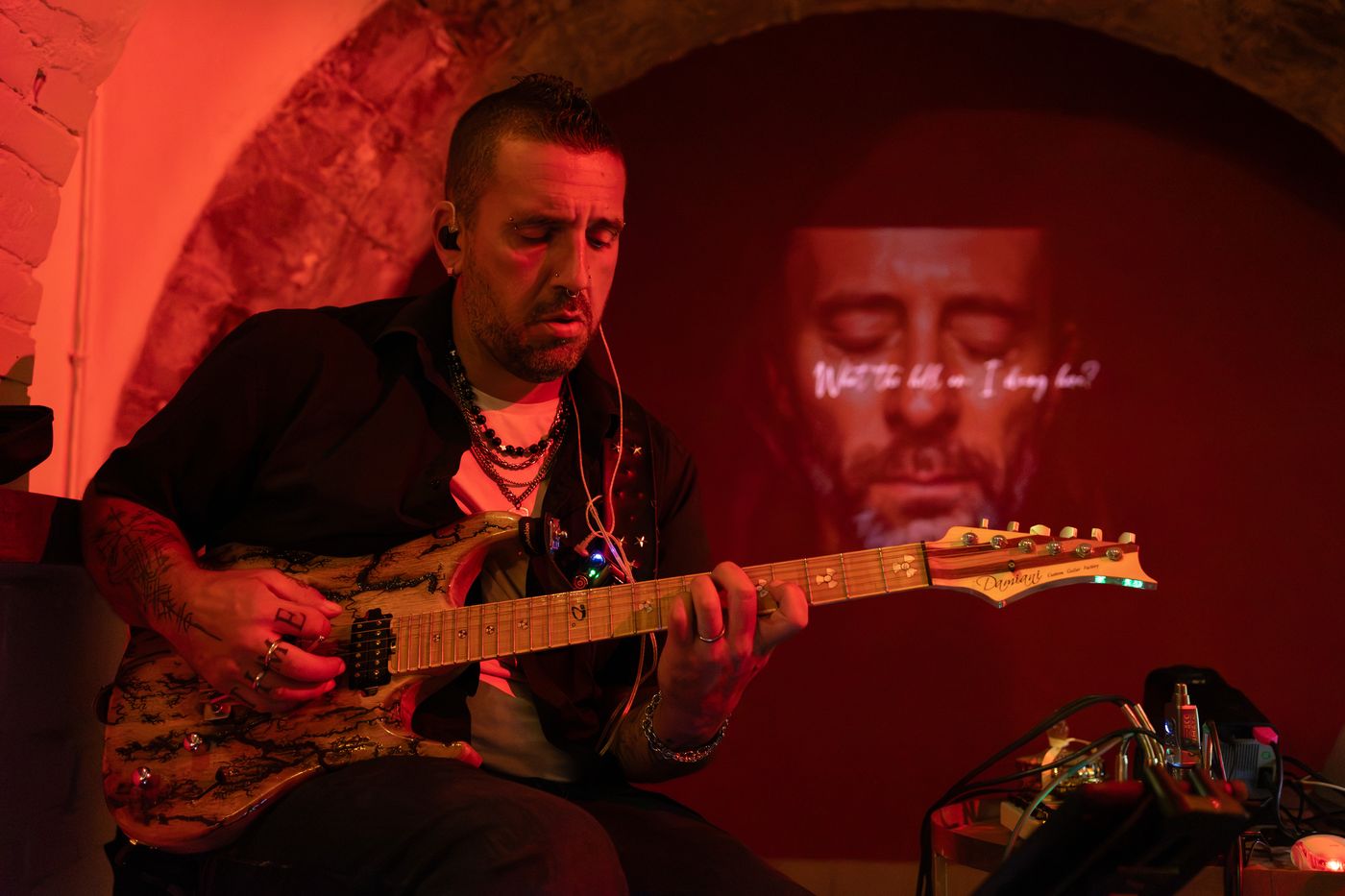 Andrea Frittelli alla chitarra elettrica; alle sue spalle è proiettato il volto animato di un artista